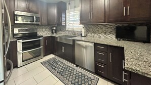 A modern kitchen with dark wood cabinets, stainless steel appliances, a tiled backsplash, and a built-in dishwasher. - US Open Pickleball Stay - 3 Masters - Walkable Location (Naples)