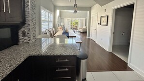 A modern kitchen with granite countertops, a built-in oven, and a dining area with a long table and chairs. - US Open Pickleball Stay - 3 Masters - Walkable Location (Naples)