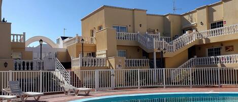 A swimming pool with a white fence, a staircase, and a building with balconies.