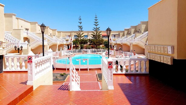 Ett semesterhotell med en pool i mitten, flera balkonger och ett klinkergolv.