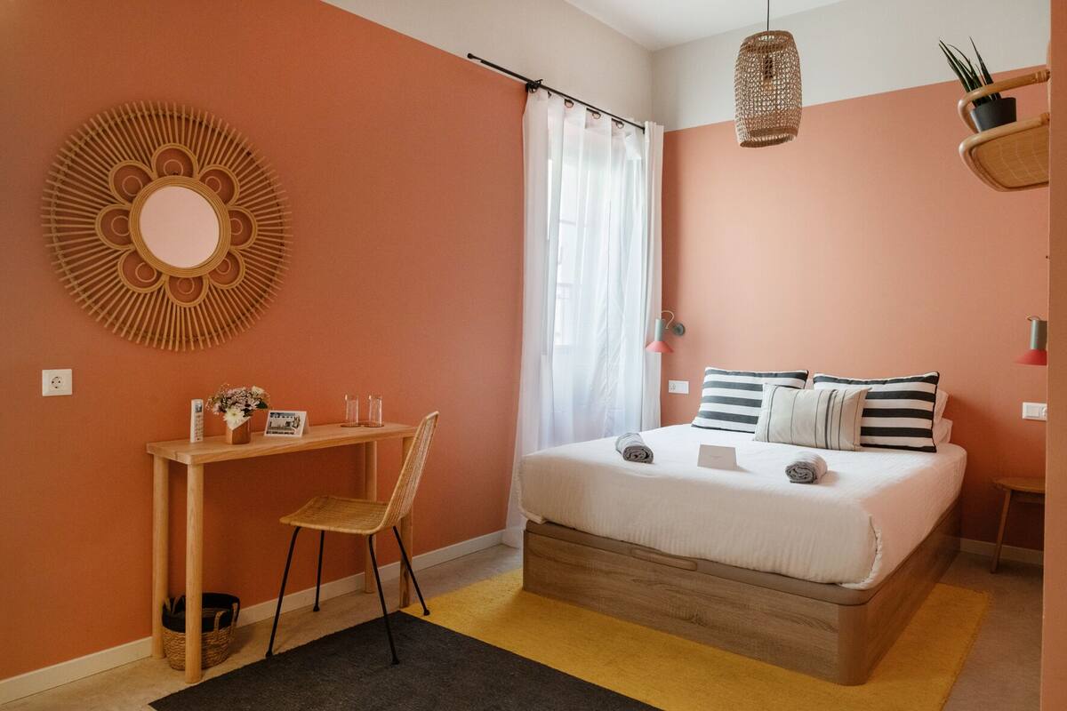 Quarto com cama, escrivaninha, cadeira, espelho e luminária pendente.