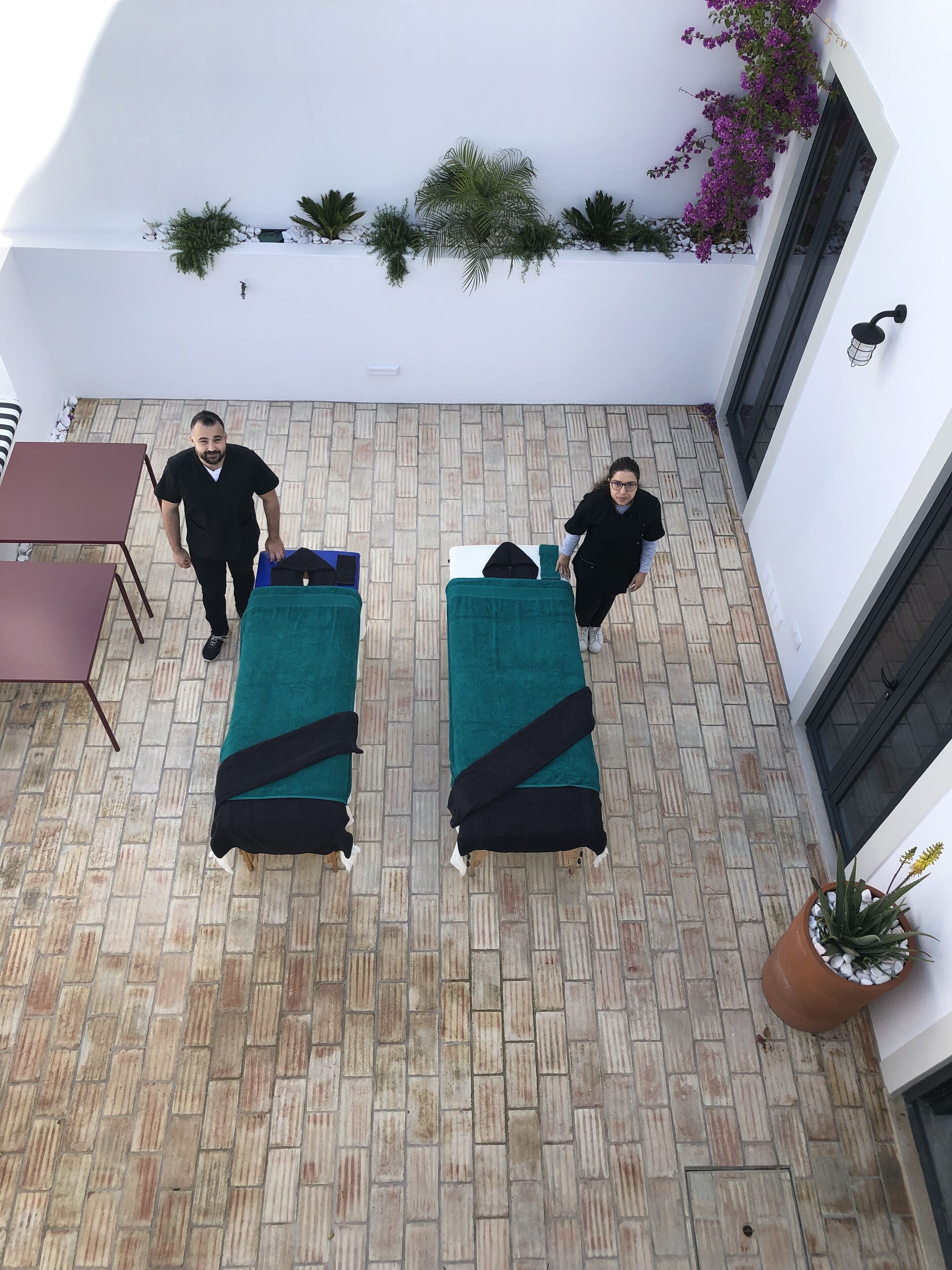 A rooftop terrace with two massage tables, a potted plant, and a brick floor.