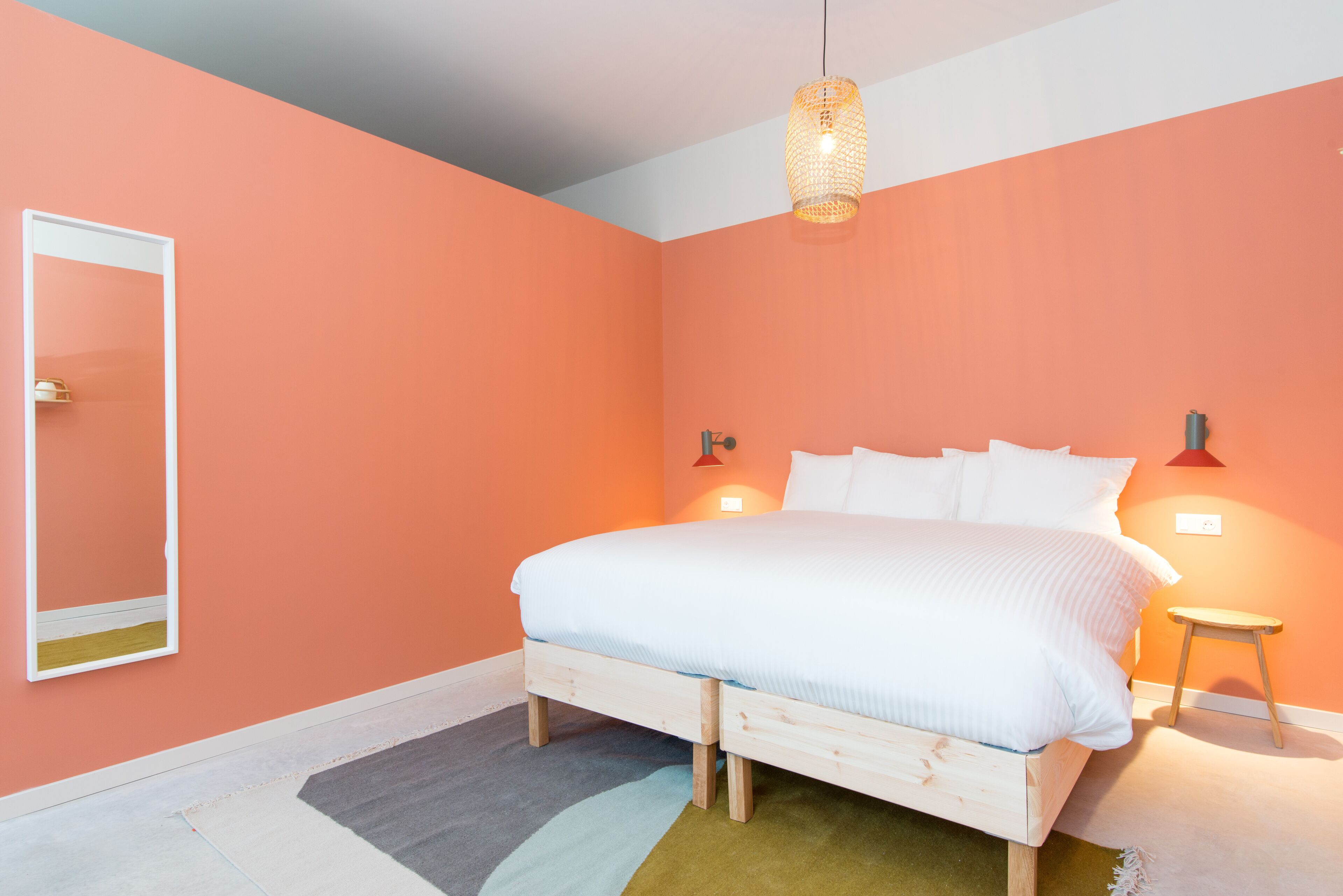 Un dormitorio con cama, una mesita de noche, una lámpara colgante y un espejo instalado en la pared.