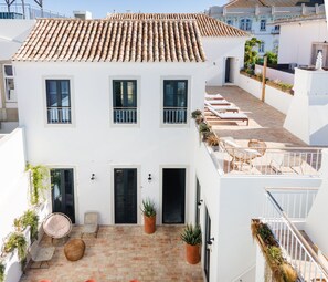 A white building with a tiled roof, a balcony with lounge chairs, and potted plants.
