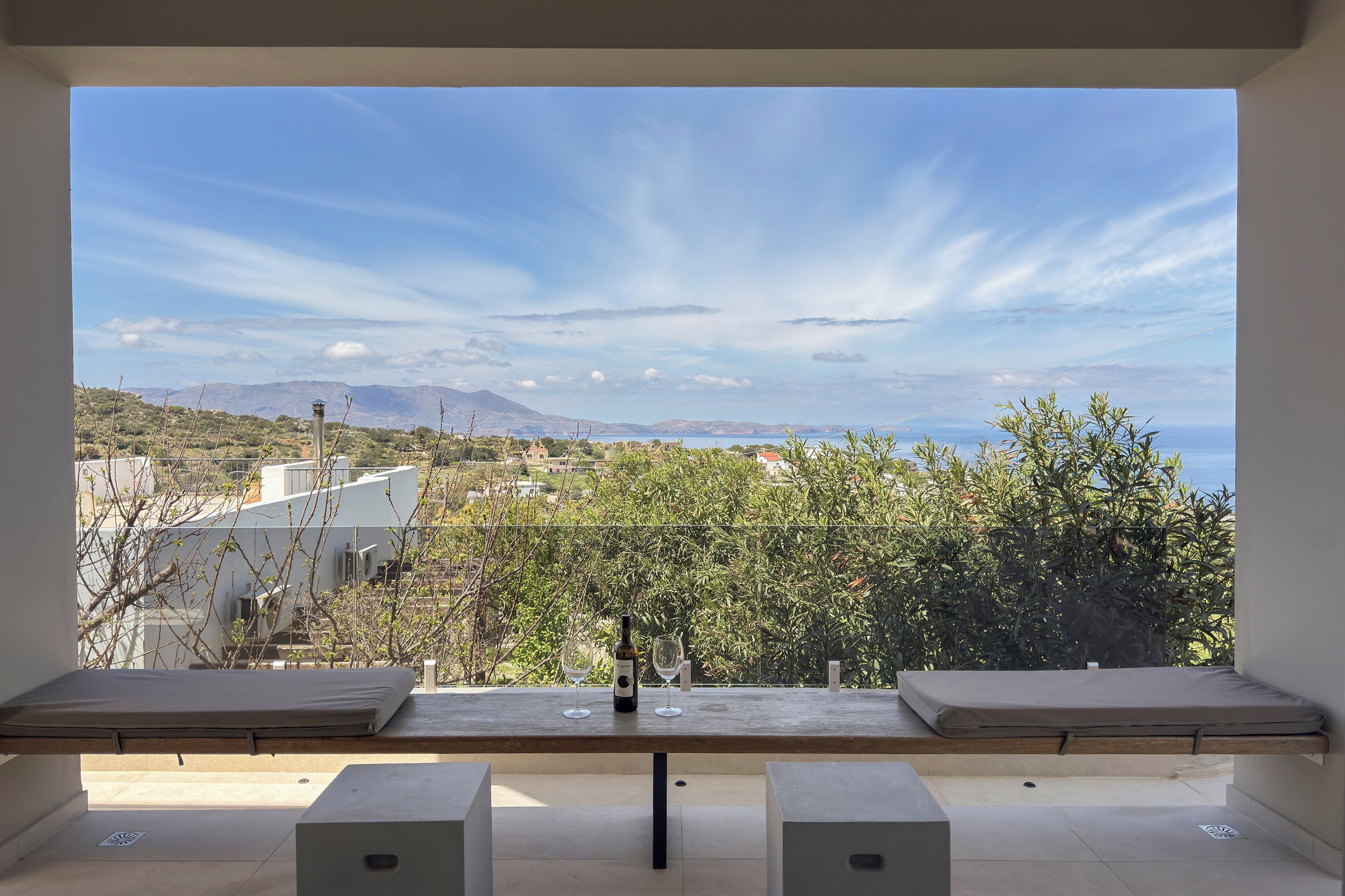 A balcony with a table, two cushioned seats, a bottle, and two glasses.