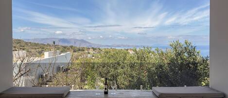 A balcony with a table, two cushioned seats, a bottle, and two glasses.