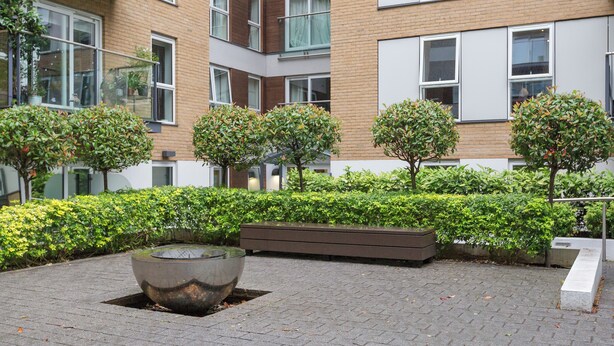 A courtyard with a large reflective water feature, neatly trimmed hedges, and a modern building with multiple windows and balconies. - Sophisticated 2 Bed Flat with Balcony in Acton (London)