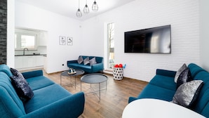 Un salon moderne avec des canapés bleus, une table basse et un téléviseur fixé sur un mur en briques blanches.