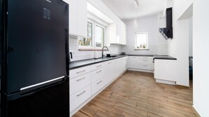 Une cuisine moderne avec des meubles blancs, un réfrigérateur noir, un plancher en bois et une fenêtre qui laisse entrer la lumière naturelle.