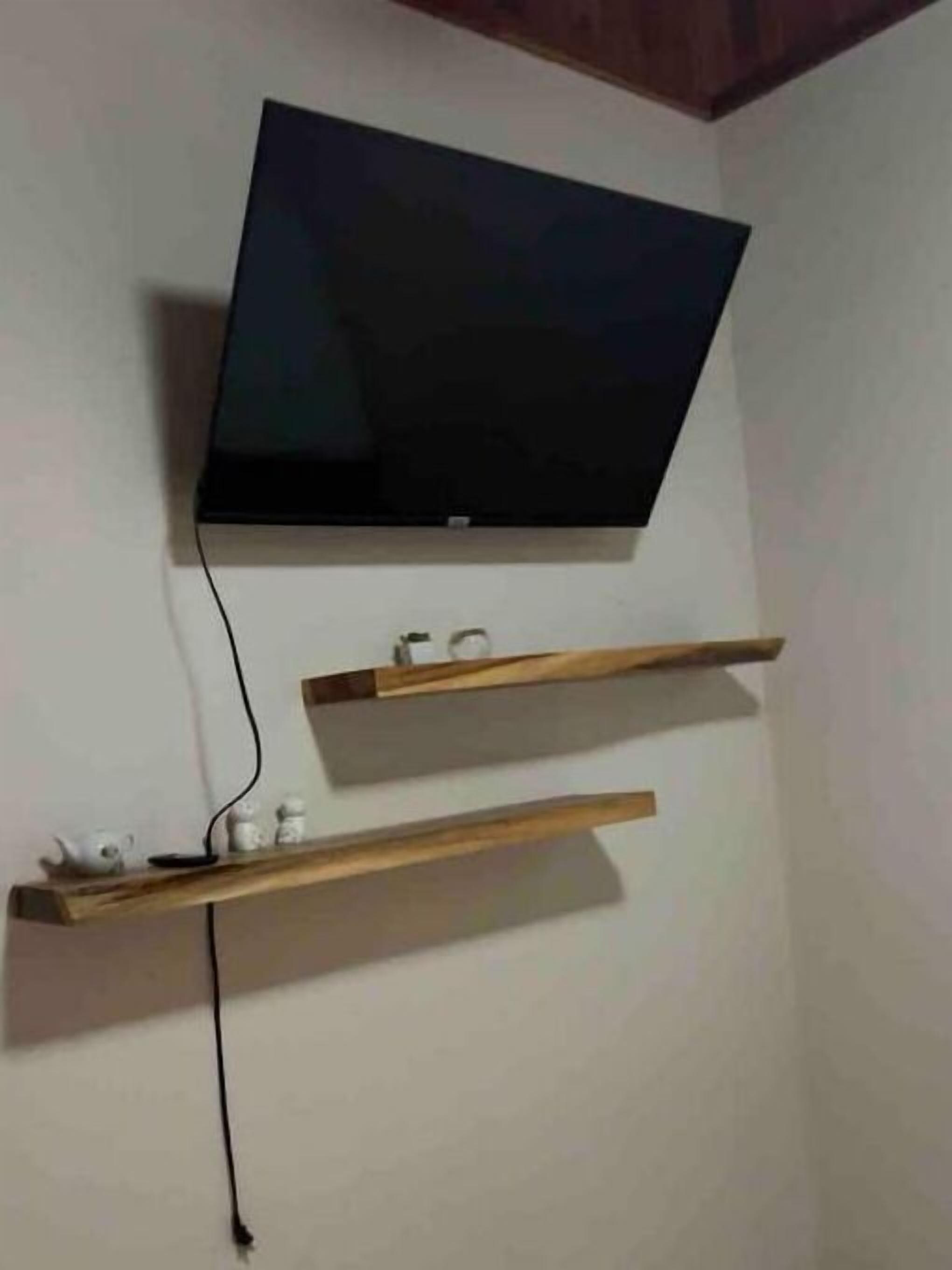 Un téléviseur à écran plat fixé au mur, avec deux étagères en bois en dessous.