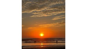 Una puesta de sol sobre una playa con olas y algunas personas a lo lejos.