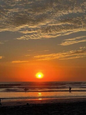 Un coucher de soleil sur l’océan, avec une plage au premier plan.