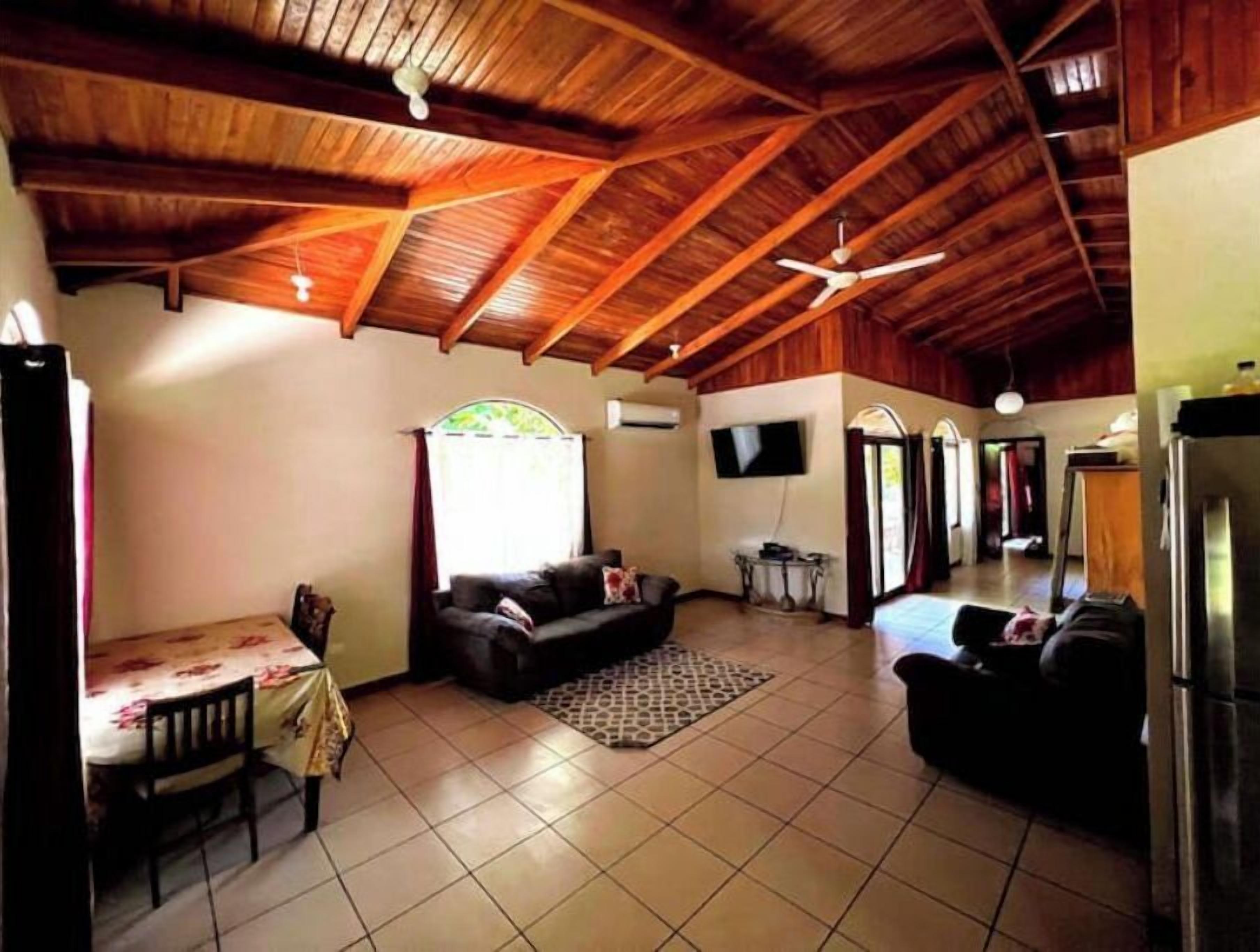 Un'ampia zona giorno con soffitto in legno a vista, un divano, una TV e un tavolo da pranzo con sedie.