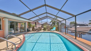 A swimming pool with a glass enclosure, surrounded by lounge chairs and a patio area.