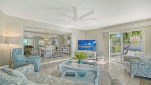 A spacious living room with a dining area, a ceiling fan, a TV, and a view of the outdoors.