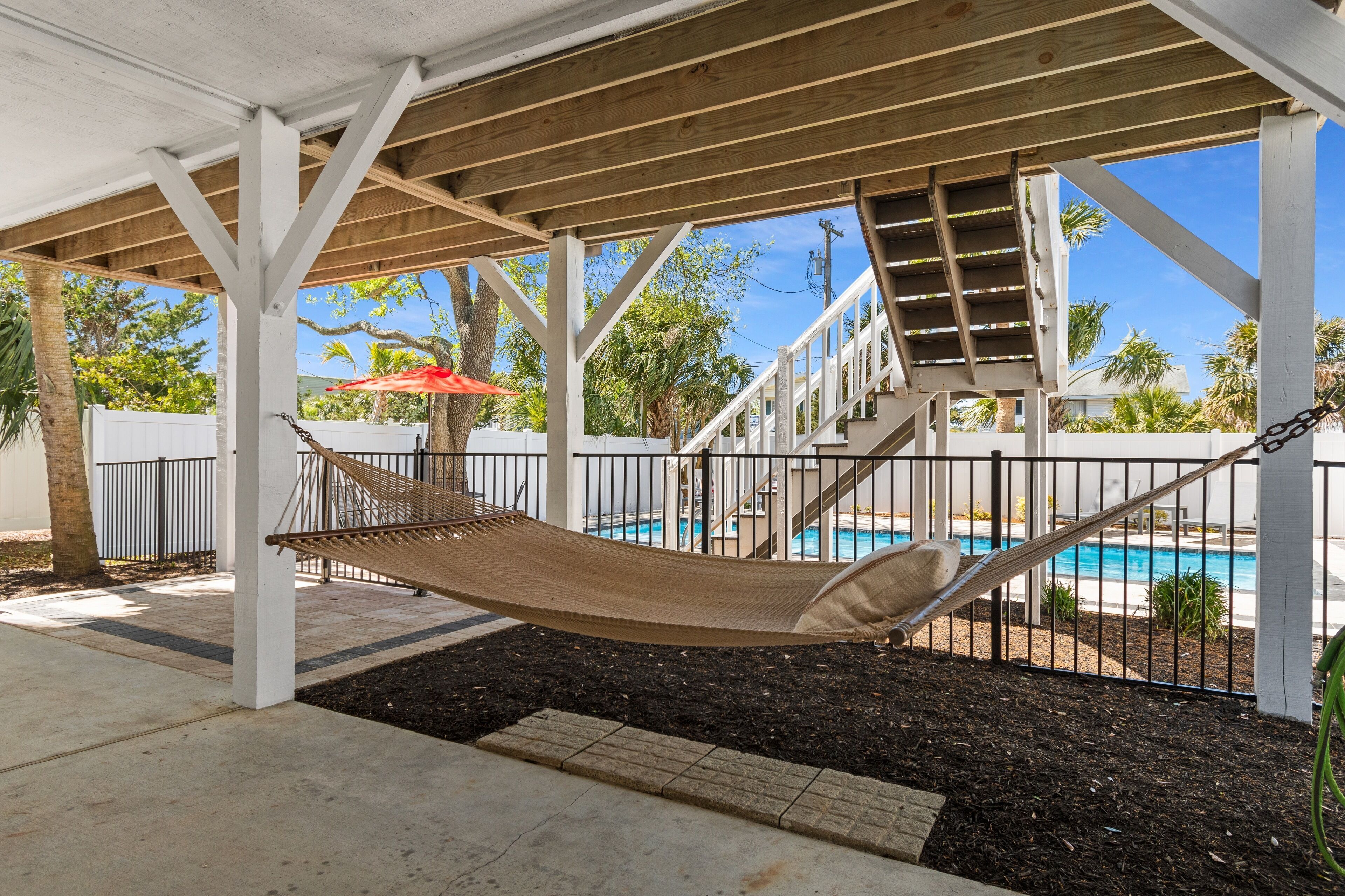 Eine Hängematte unter einer Hollaube mit einem Pool und Treppen im Hintergrund.