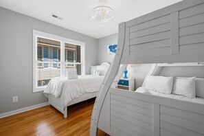 A bedroom with a bunk bed, a single bed, a window with blinds, a ceiling light, and a nightstand with a lamp.