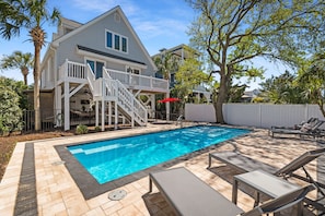 A swimming pool with lounge chairs, a staircase to a deck, and a white fence.