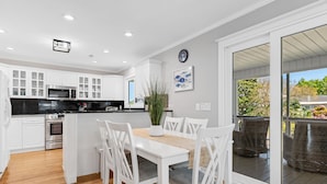 A modern kitchen with white cabinetry, a central island, and a dining area with white chairs. - Garden City Retreat with Pool, Walk to Beach (Garden City Beach)