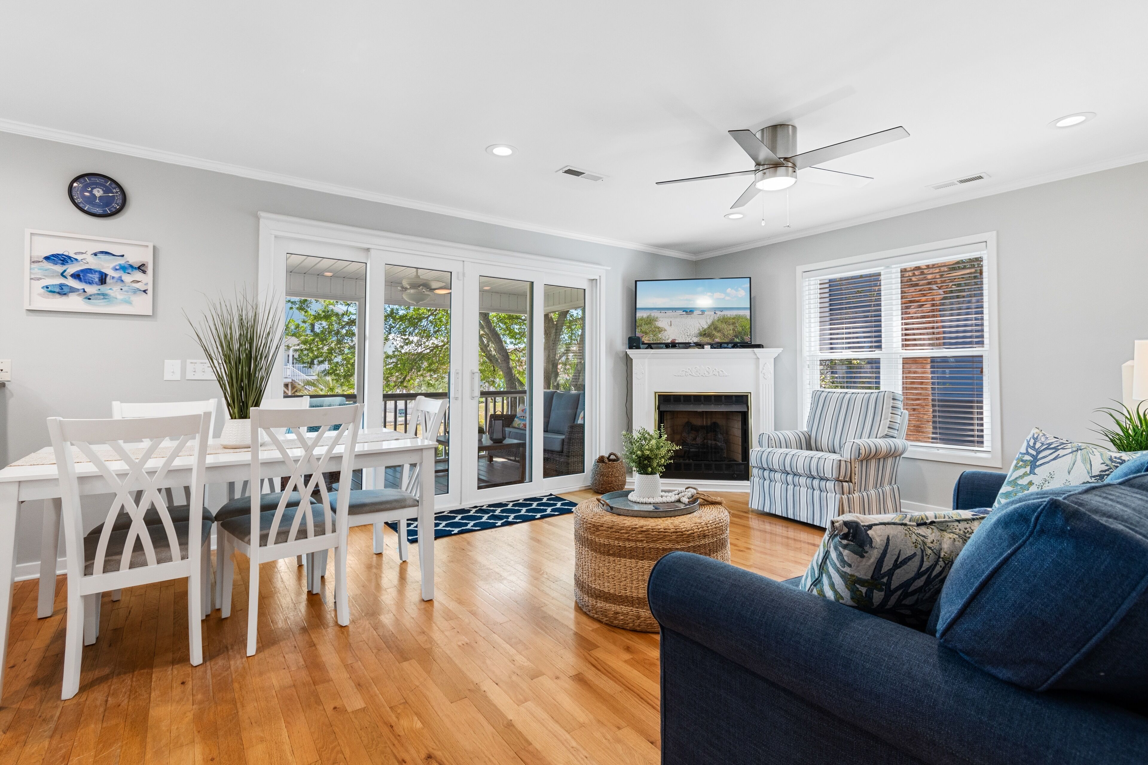 A spacious living room with a fireplace, a dining area with white furniture, and a large window with blinds.