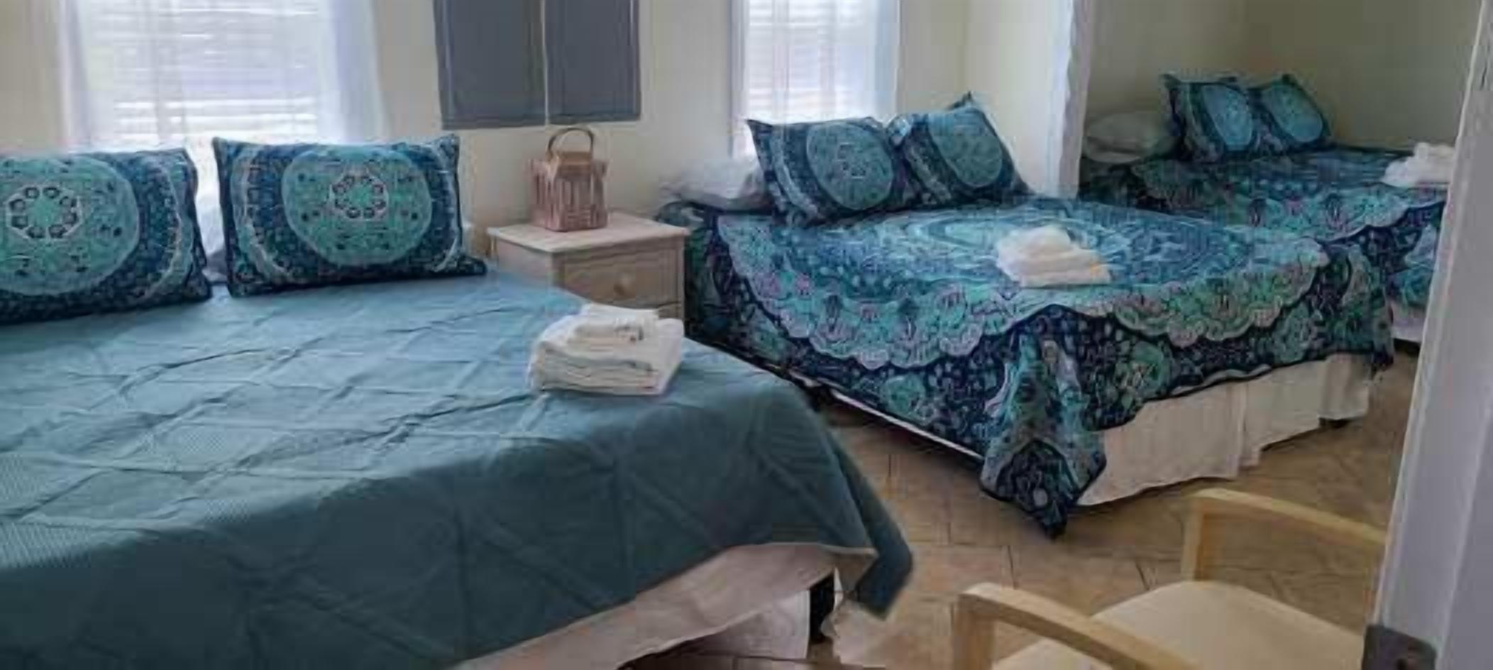 A bedroom with two beds, each with a blue patterned bedspread and matching pillows. There is a nightstand with a lamp between the beds.