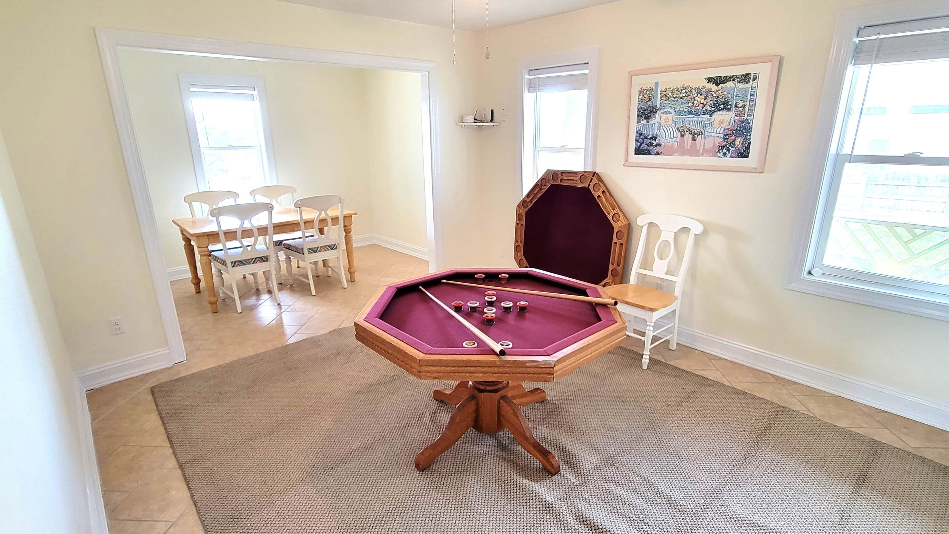 Une pièce avec une table de billard, un coin repas avec des chaises et un tableau accroché au mur.