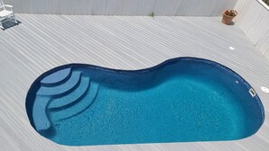 Une piscine dont le bord est revêtu de carreaux, entourée d’une terrasse en bois.