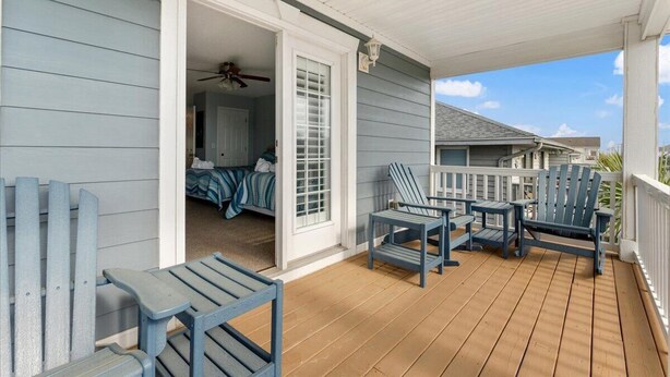 Een overdekte veranda met Adirondack-stoelen en een bed zichtbaar door een geopende deur.