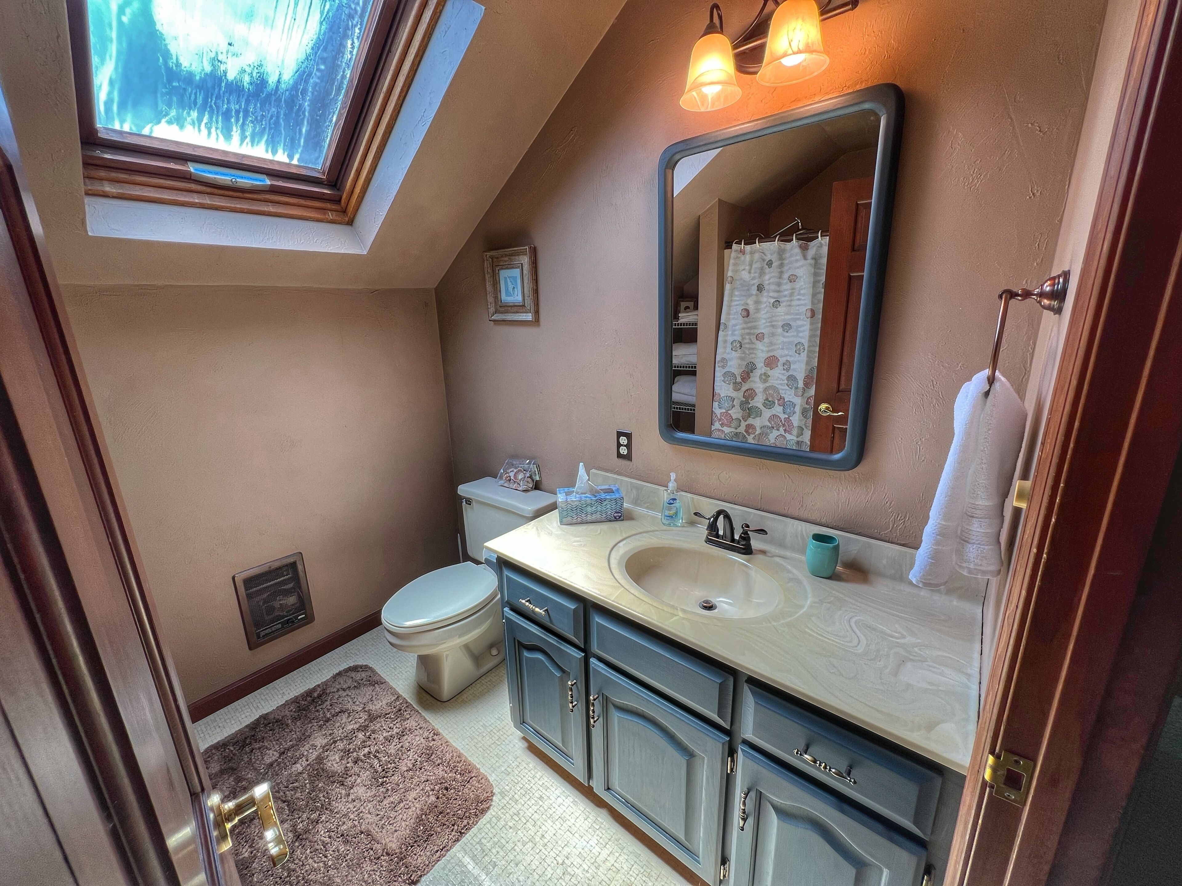 A bathroom with a skylight, a toilet, a sink with a mirror, and a towel rack.