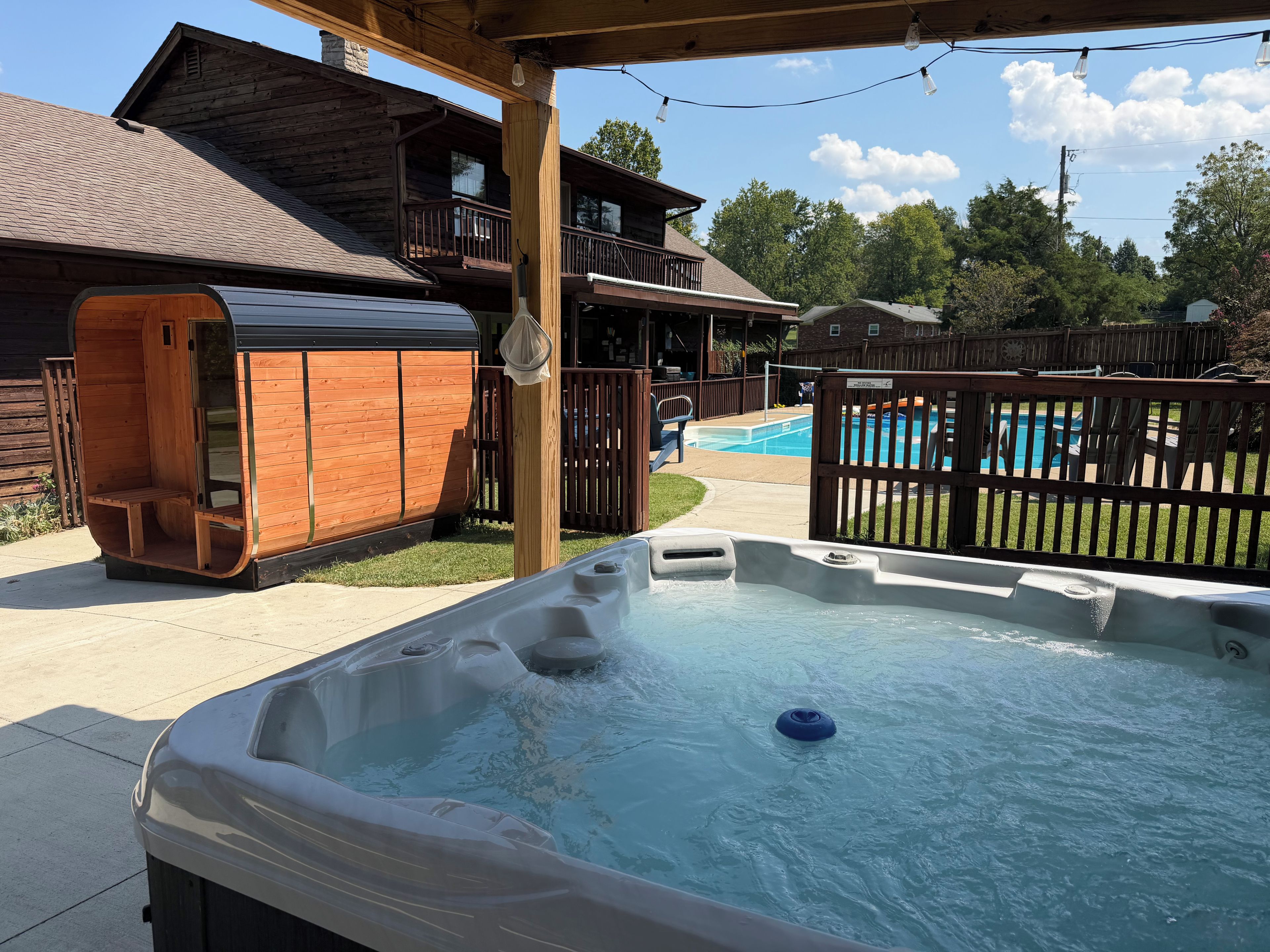 Un jacuzzi con terraza de madera y piscina al fondo.