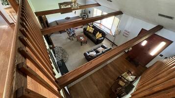 Un vaste espace de vie doté d’un haut plafond, d’un escalier en bois et d’un ventilateur de plafond.