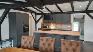 A modern kitchen with a central island, dark cabinetry, and a dining area with a wooden table and tufted chairs. - Apartment "Speicher-Loft" (Klein Upahl)