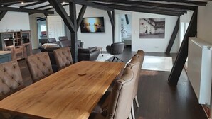A spacious dining area with a long wooden table and leather chairs, a kitchen in the background, and a view of the living room through an open archway. - Apartment "Speicher-Loft" (Klein Upahl)