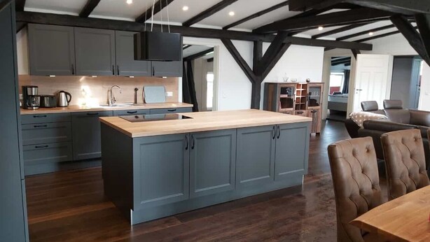 A modern kitchen with grey cabinets, a wooden island, and a dining area with leather chairs. - Apartment "Speicher-Loft" (Klein Upahl)