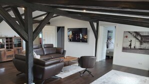 A spacious living room with a dark wooden floor, a leather sofa, a coffee table, and a large rug. There is a TV mounted on the wall and a painting above it. - Apartment "Speicher-Loft" (Klein Upahl)