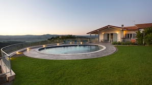 A swimming pool with a surrounding deck, a covered patio, and a view of distant hills.