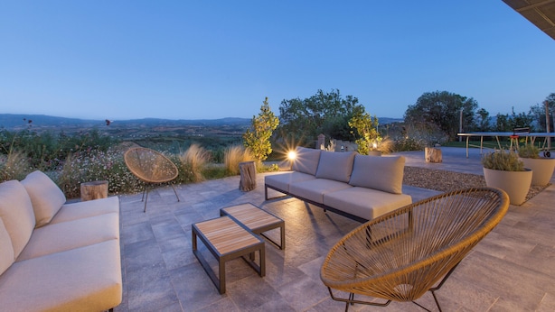 An outdoor seating area with a sofa, chairs, and tables, overlooking a scenic landscape.