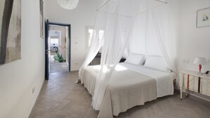 A bedroom with a canopy bed, a bedside table with a lamp, and a view of a hallway.