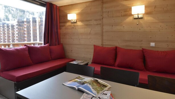 A cozy room with a wooden wall, two red sofas, a table with magazines, and two wall-mounted lights. - 100m from resort center, 3rd floor, view ski slopes, swimming pool, balcony, tv, ski locker, 35m² (La Plagne)
