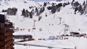 A ski resort with a ski lift, ski slopes, and a wooden building. - 100m from resort center, 3rd floor, view ski slopes, swimming pool, balcony, tv, ski locker, 35m² (La Plagne)