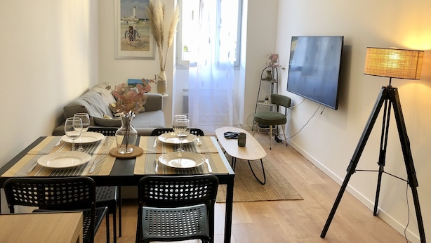 En matplats med ett bord dukat för fyra personer, en soffa, en tv och en lampa.