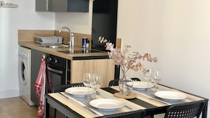 Ett kompakt kök med diskho, spis och en matplats för två personer, komplett med tallrikar och glas.
