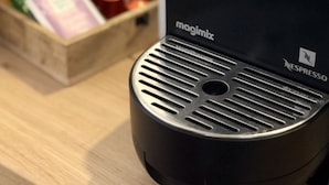 En kaffemaskin med ett varumärkesmärke från Magimix, en Nespresso-logotyp och en trälåda med diverse föremål i bakgrunden.