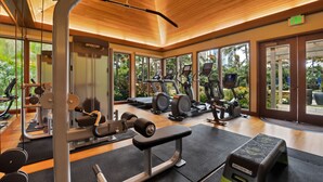 Ein modernes Fitnessstudio mit verschiedenen Trainingsgeräten, großen Fenstern und einer Holzzieldecke.