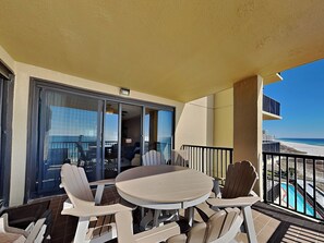 Un balcon avec une table ronde et des chaises, une vue sur la plage et un bâtiment en arrière-plan.