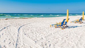 Ein Strand mit weißem Sand und blauem Himmel. Blaue und gelbe Liegen und Sonnenschirme sind vorhanden.
