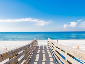 A wooden boardwalk leading to a beach with a clear blue sky.