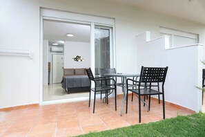 Una veranda esterna con tavolo e sedie, una porta scorrevole in vetro che dà su un ambiente interno, e una piccola area verde sullo sfondo.