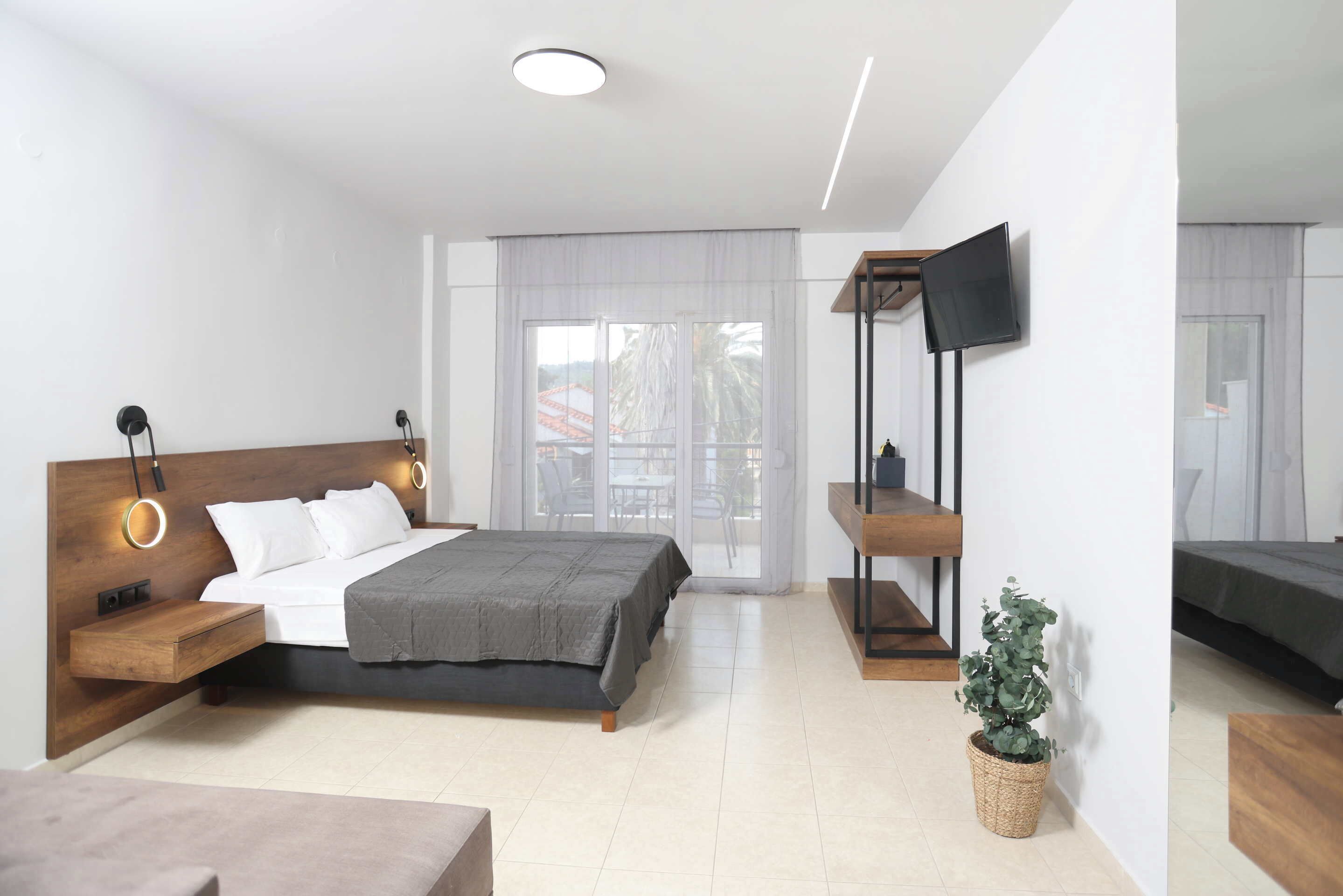 Een moderne slaapkamer met een bed, nachtkastjes, een televisie en een potplant.