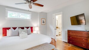 Un dormitorio con una cama grande, ventilador de techo, televisor y cómoda de madera.
